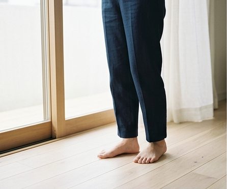 窓辺の床に素足で立つ女性を膝から下だけ写した写真